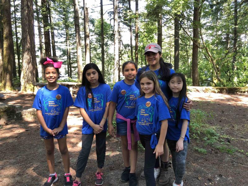 A camp leader and 5 campers, all girls wearing blue t-shirts, face the camera.