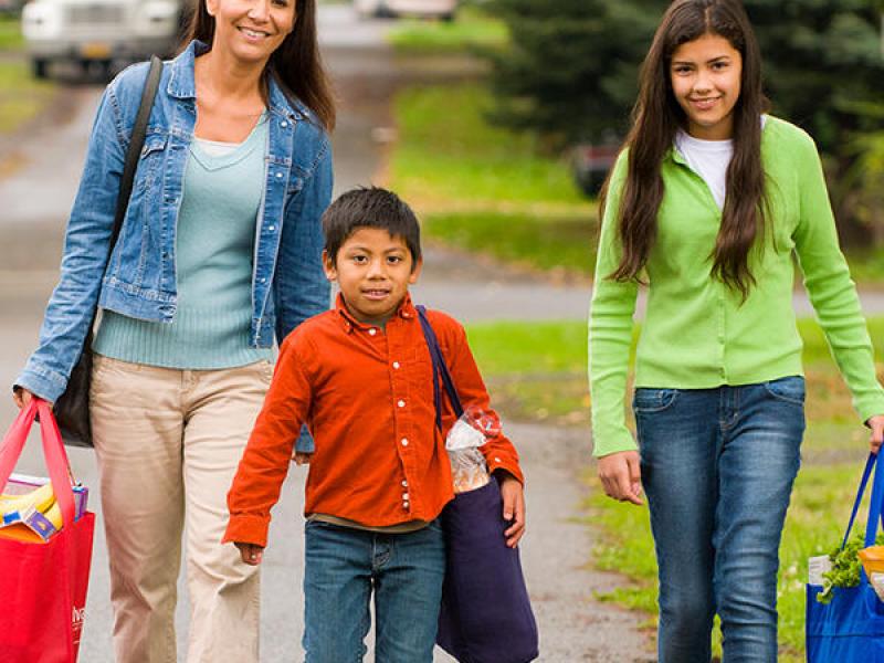 A mother, daughter and son carry groceries in reusable bags.