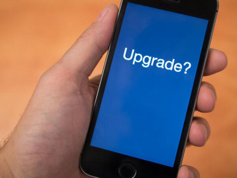 A hand holds a cell phone. The screen asks the question, "upgrade?"