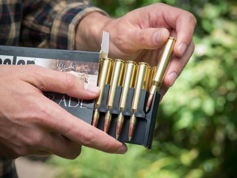 A close-up of a pair of hands examining copper bullets in a rifle magazine.