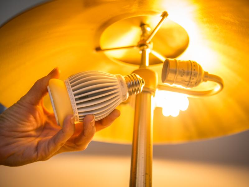 A hand is holding an LED lightbulb next to a lamp with an extra light bulb socket.