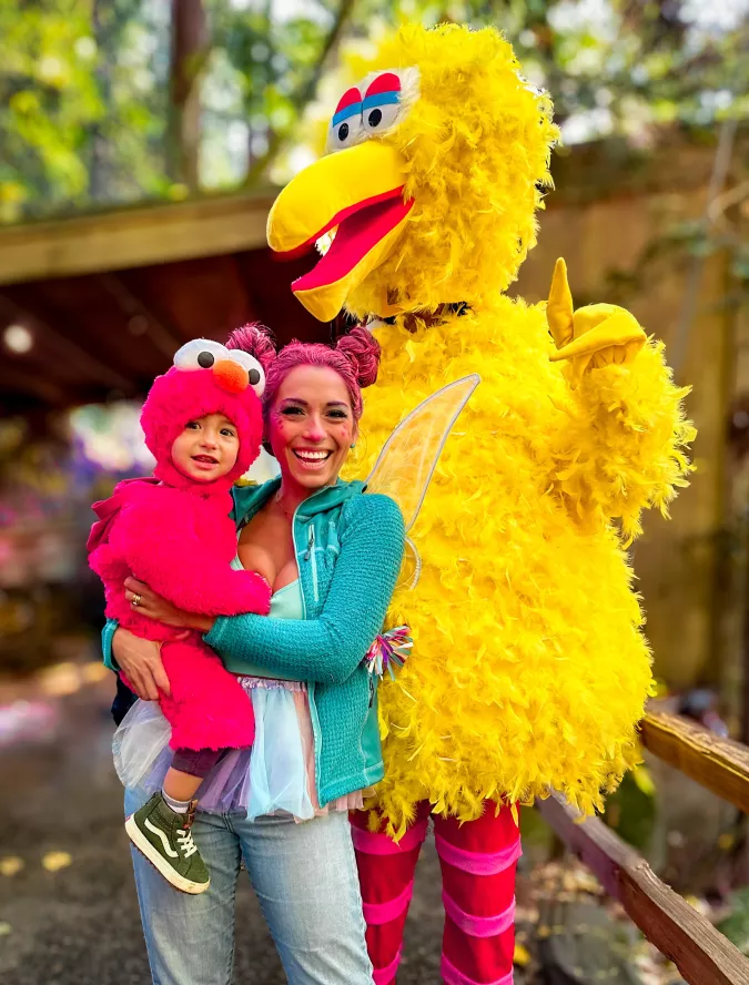 woman dressed as Abby Cadabby holding child dressed as Elmo standing next to Big Bird